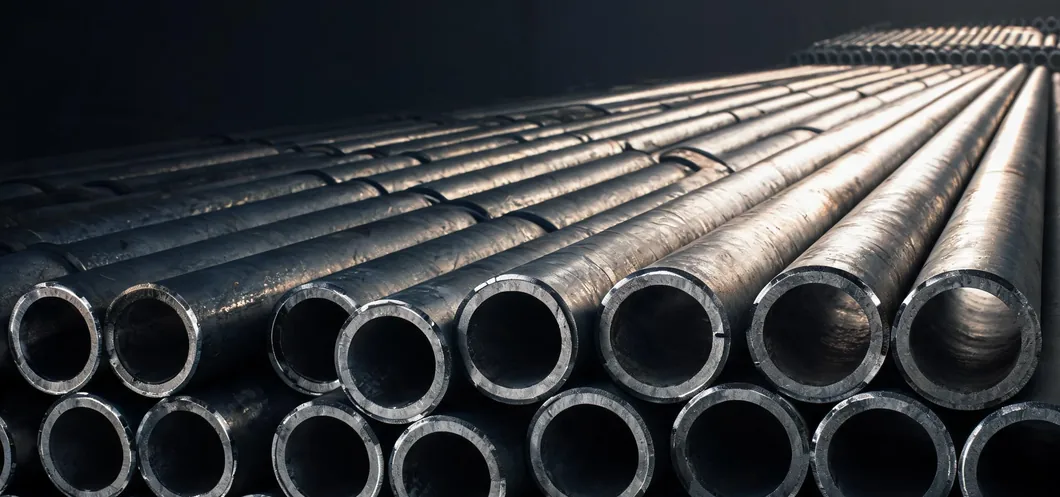 Rows of large-diameter steel pipe stacked on a dark floor, cut ends and wall thickness facing the camera